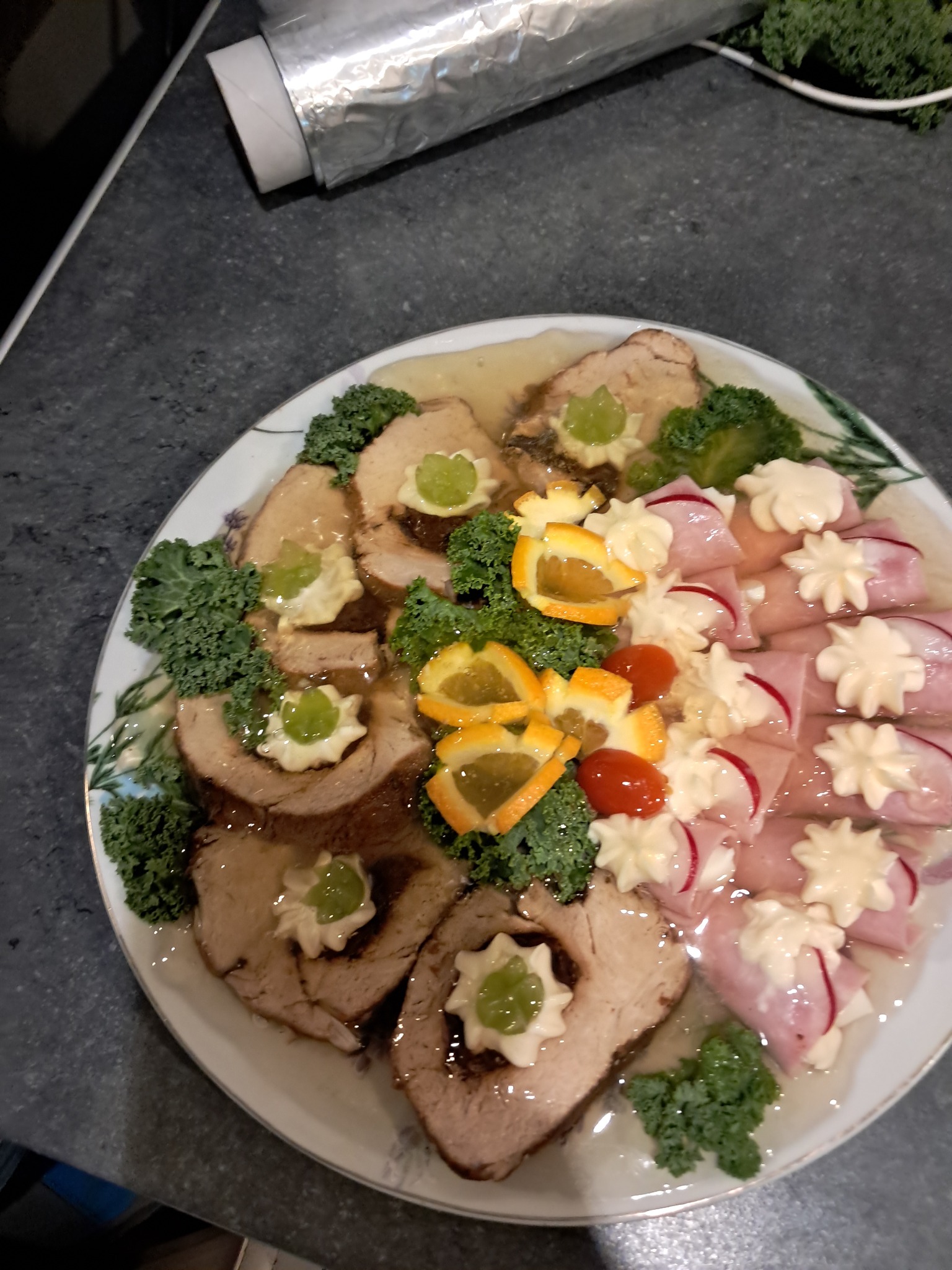 Wykwintna galaretka z mięsem, szynką i warzywami na białym talerzu z delikatnym wzorem, prezentująca elegancką kompozycję kulinarną na przyjęcie.