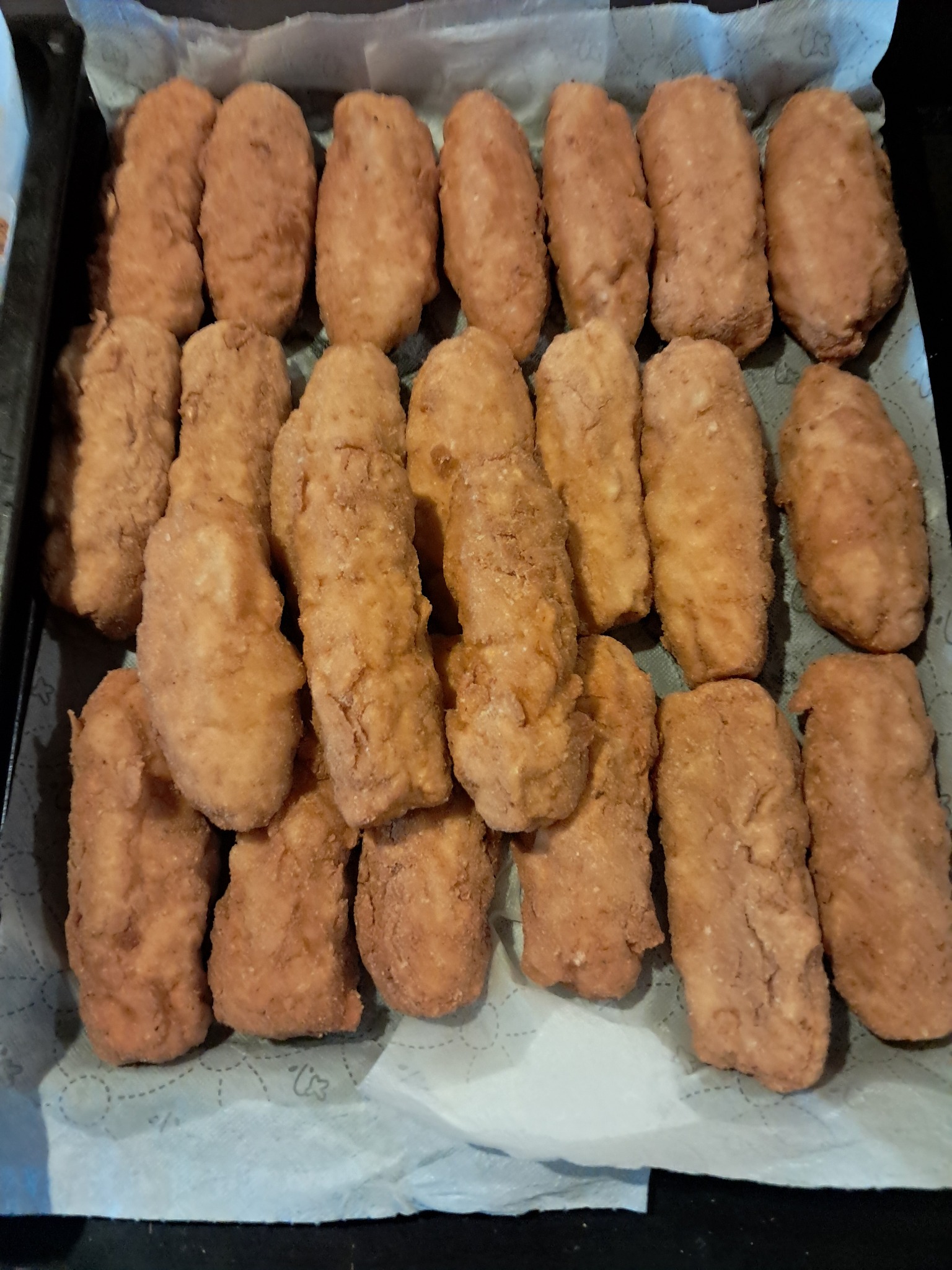 Rządki smażonych krokietów na blasze wyłożonej papierem do pieczenia. Domowy wyrób garmażeryjny z chrupiącą panierką w ciepłych odcieniach brązu.