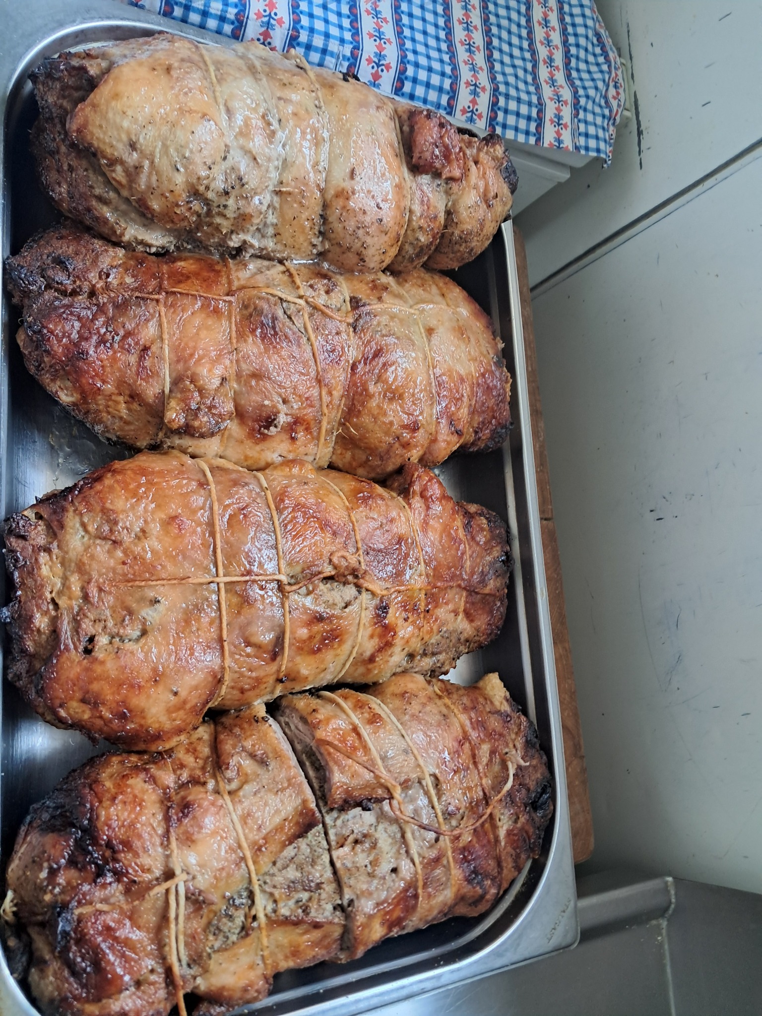 Cztery pieczone rolady mięsne, związane sznurkiem, ułożone na metalowej tacy. Jedna z rolad jest częściowo pokrojona. W tle widoczna kraciasta ściereczka.
