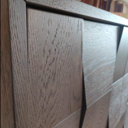 Styl mebel - Fragment szafy z ciemnego drewna z geometrycznym wzorem 3D na frontach, widoczne usłojenie drewna i precyzyjne połączenia elementów.