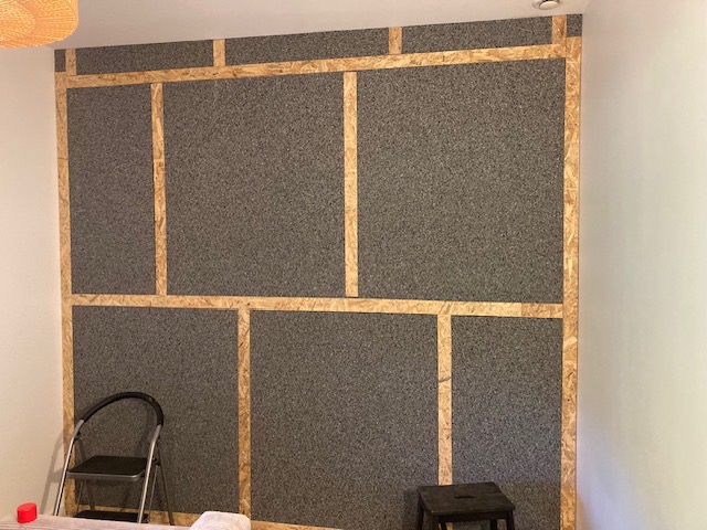 Wnętrze w trakcie prac: izolacja akustyczna ściany z płyt OSB i szarej wełny mineralnej, widoczna drabina i stołek.