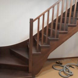 P.P.H.U.Heban - Wykonane z ciemnego drewna schody z balustradą, z zakrętem u dołu, w trakcie prac wykończeniowych, widoczny odkurzacz przemysłowy i wkrętarka.