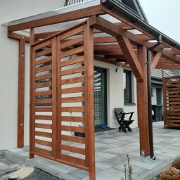 P.P.H.U.Heban - Zadaszenie tarasu z drewnianą konstrukcją i ażurowymi ściankami bocznymi, widoczne rynny, szara kostka brukowa i fragment domu.