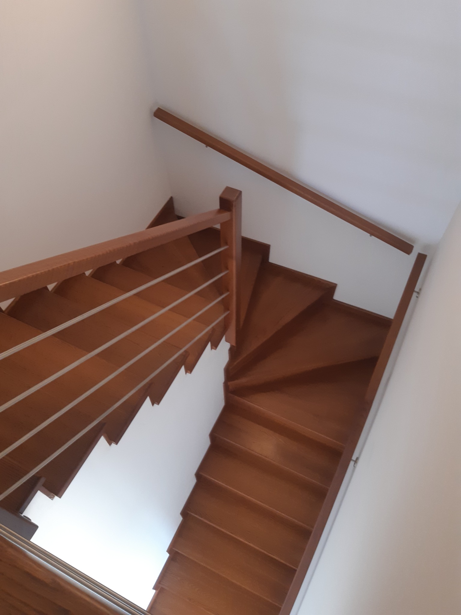 Wewnętrzne, spiralne schody z drewna z metalowymi prętami balustrady, widok z góry, jasne wnętrze.