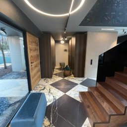 VOLTA - Nowoczesny hol z marmurową podłogą w szachownicę, drewnianymi schodami i szafami w zabudowie, oświetlony okrągłą lampą LED i z dekoracyjnym malowidłem na suficie.