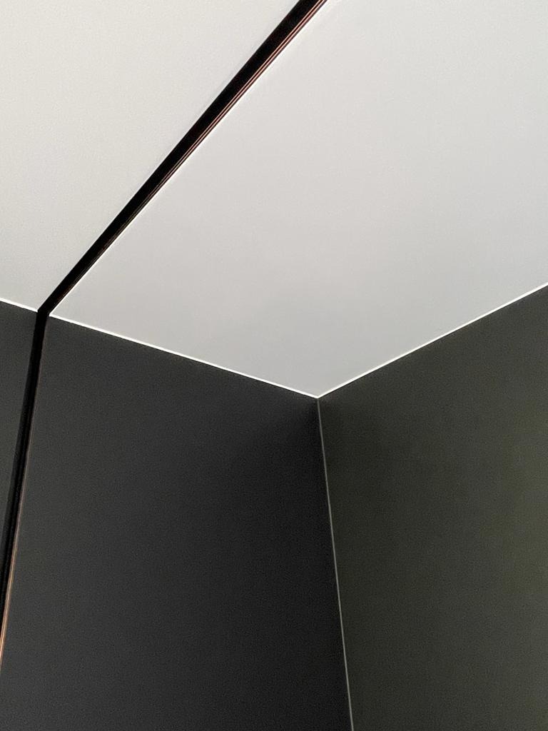 Nowoczesne wykończenie wnętrza: połączenie gładkiej, białej płyty karton gips na suficie z ciemnoszarymi ścianami, podkreślone minimalistyczną listwą.