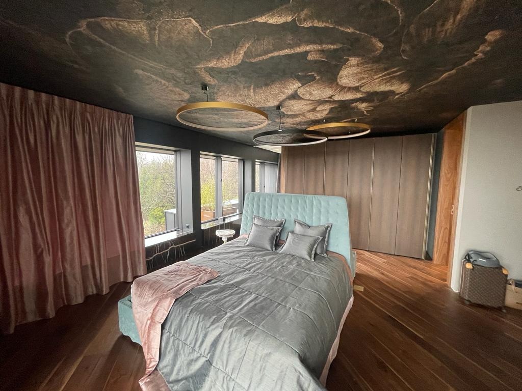 Sypialnia z niestandardowym malowaniem sufitu imitującym abstrakcyjne chmury, okrągłe lampy wiszące i łóżko z turkusowym zagłówkiem, parkiet w jodełkę.