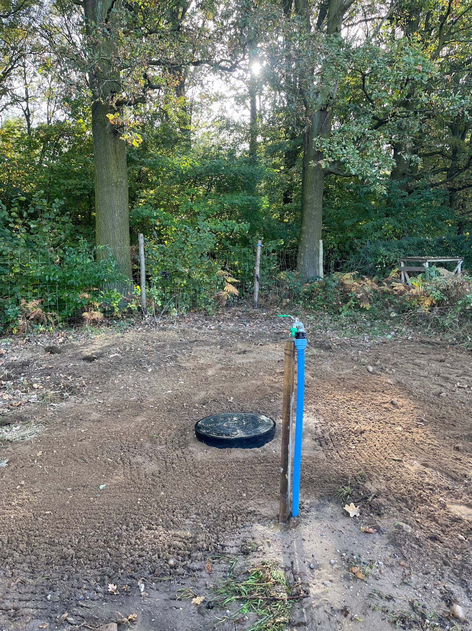 Zakończony montaż studni z niebieską rurą i kranem na tle leśnym z ogrodzeniem z siatki.