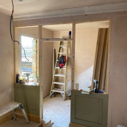 LewBud - Wnętrze w trakcie remontu: ściany otynkowane, drewniane konstrukcje ścianek działowych, drabina, narzędzia i materiały budowlane widoczne w pomieszczeniu.