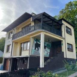 LewBud - Dwupiętrowy dom z balkonem i muralem przedstawiającym niedźwiedzie na elewacji, widok z dołu na tle zieleni.