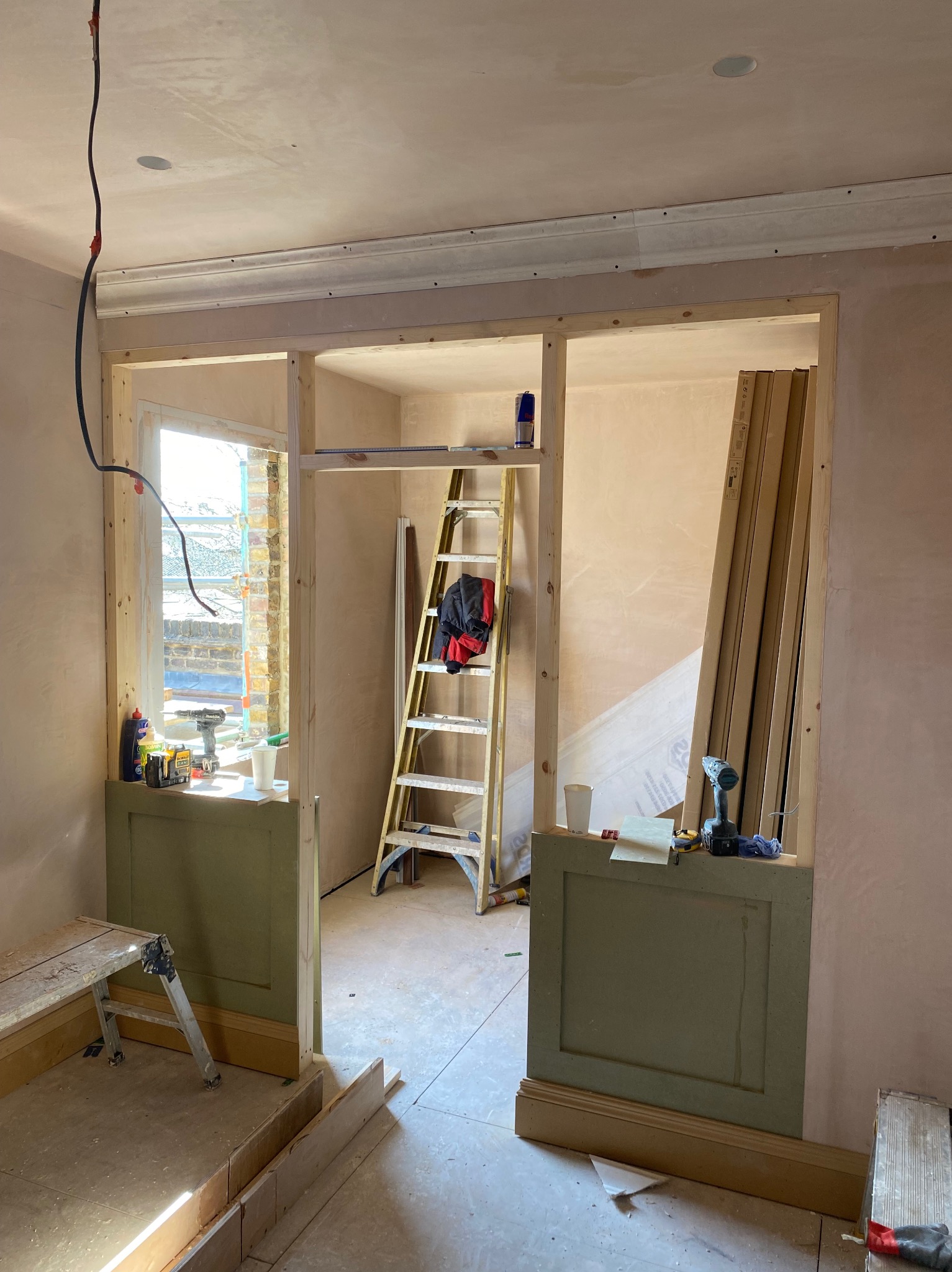 Wnętrze w trakcie remontu: ściany otynkowane, drewniane konstrukcje ścianek działowych, drabina, narzędzia i materiały budowlane widoczne w pomieszczeniu.