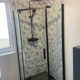 Nowoczesna kabina prysznicowa z czarnymi ramami i deszczownicą, zamontowana w łazience z płytkami w motywy morskie.