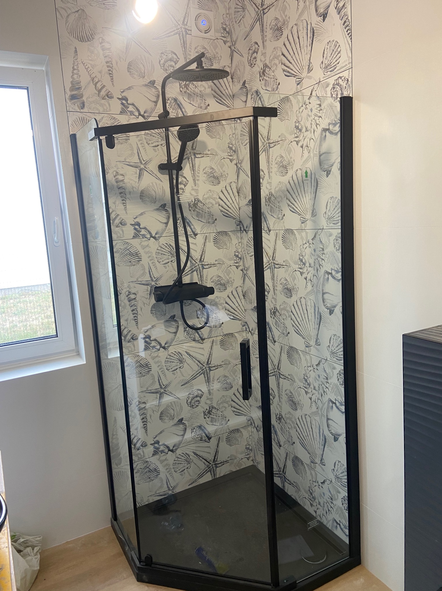 Nowoczesna kabina prysznicowa z czarnymi ramami i deszczownicą, zamontowana w łazience z płytkami w motywy morskie.