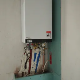 Nowy piec gazowy Viessmann zamontowany na ścianie z płyt kartonowo-gipsowych, z widocznymi rurami i przewodami izolowanymi pianką montażową w kolorach czerwonym i niebieskim.