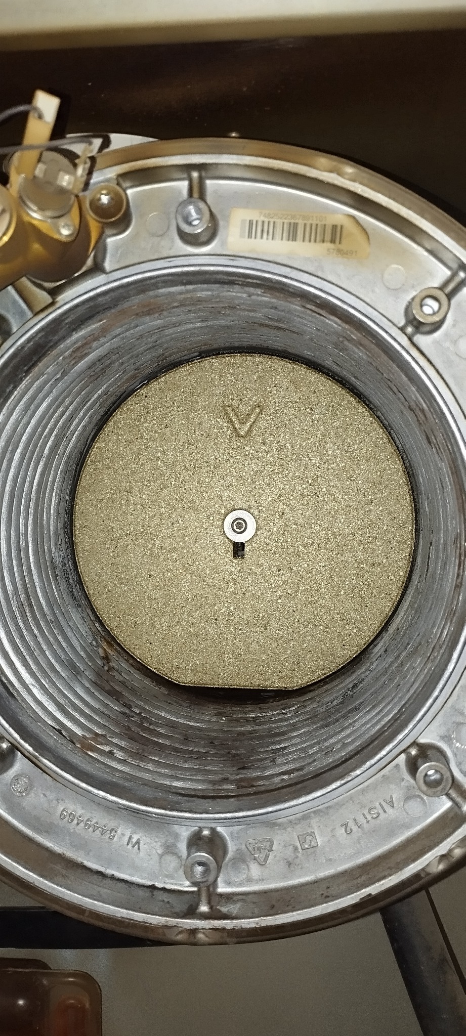 Wnętrze pieca gazowego z widocznym palnikiem, ujęcie z góry ukazujące metalową obudowę z żebrowaniem i okrągły palnik z centralnie umieszczonym otworem oraz symbolem strzałki w dół na powierzchni...