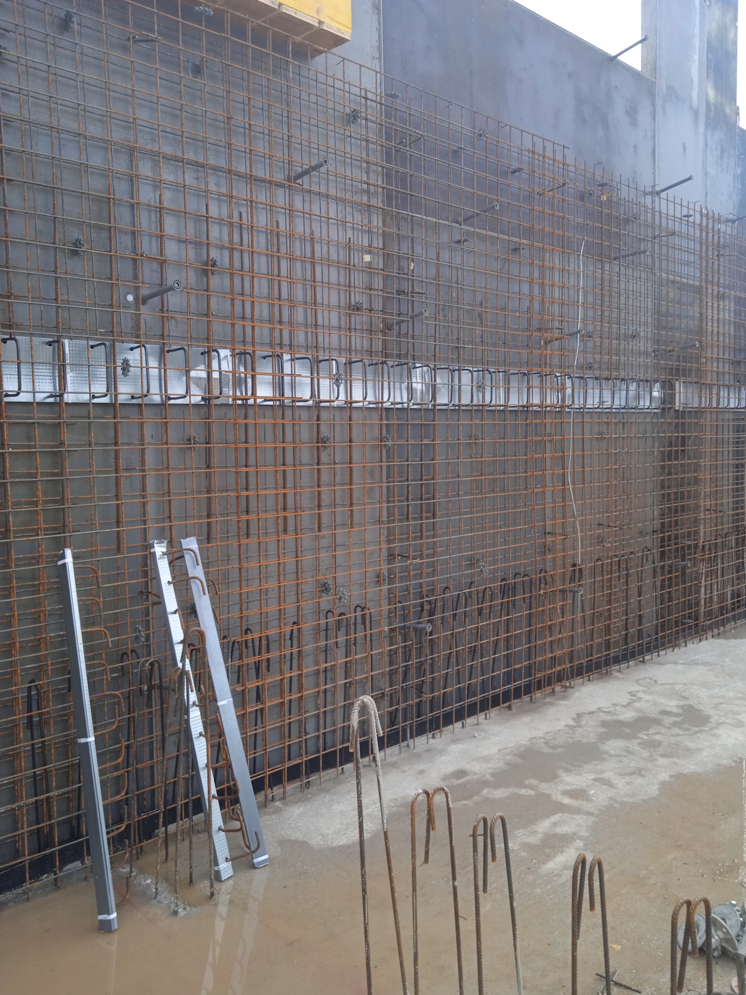 Zbrojenie pionowej ściany fundamentowej z widocznymi elementami dystansowymi i fragmentami szalunku. Prace przygotowawcze do betonowania.