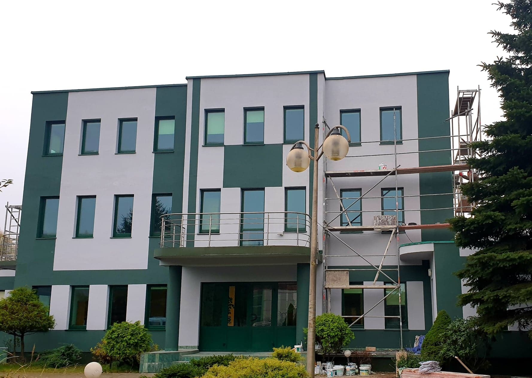 Budynek w Warszawie z fragmentem rusztowania podczas malowania elewacji na zielono i szaro, widoczne puszki z farbą.