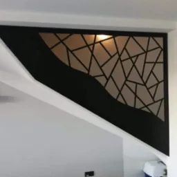 Nowoczesna, czarna barierka schodowa z geometrycznym wzorem i falistym elementem dekoracyjnym, zamontowana przy białych schodach w minimalistycznym wnętrzu.