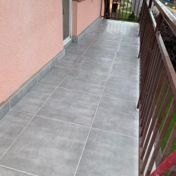 Błażej Wychodzki - Wykończony balkon z szarymi płytkami podłogowymi i brązową balustradą, widok z góry, ściana w kolorze pudrowego różu.