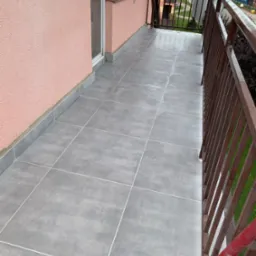 Wykończony balkon z szarymi płytkami podłogowymi i brązową balustradą, widok z g&oacute;ry, ściana w kolorze pudrowego r&oacute;żu.