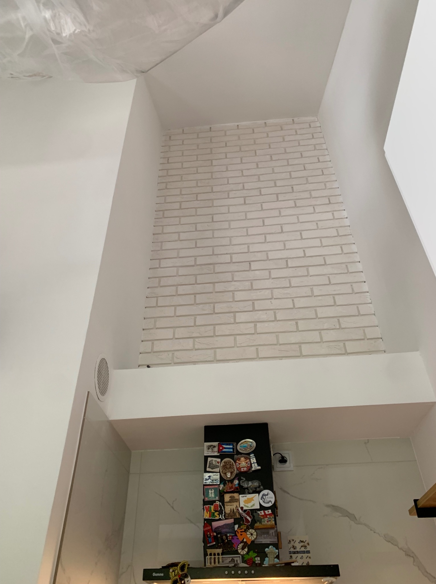 Wykończona ściana w kuchni z białej cegły, okap z magnesami na lodówce, białe ściany i sufit z folią ochronną, widok z dołu.