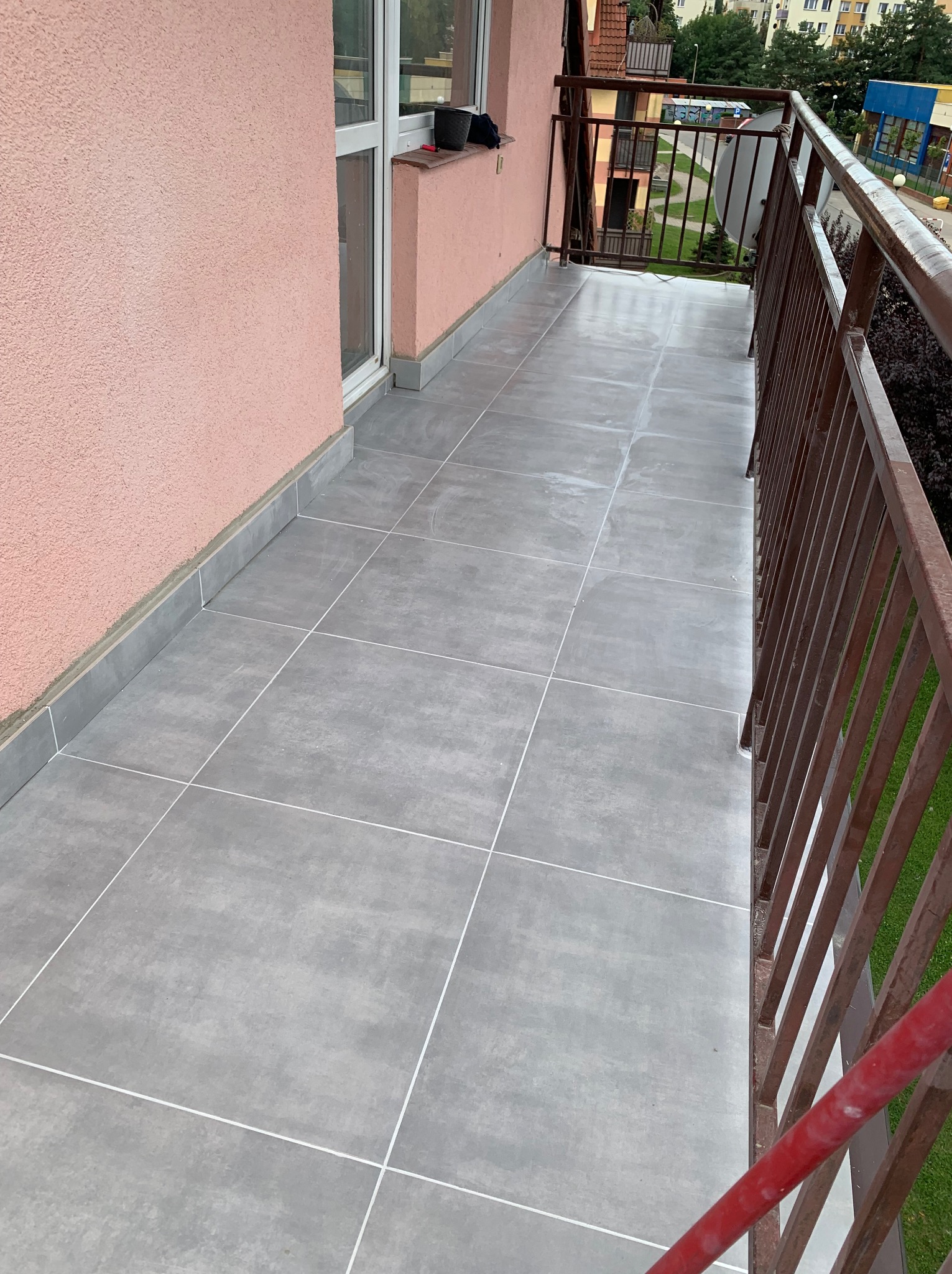 Wykończony balkon z szarymi płytkami podłogowymi i brązową balustradą, widok z góry, ściana w kolorze pudrowego różu.