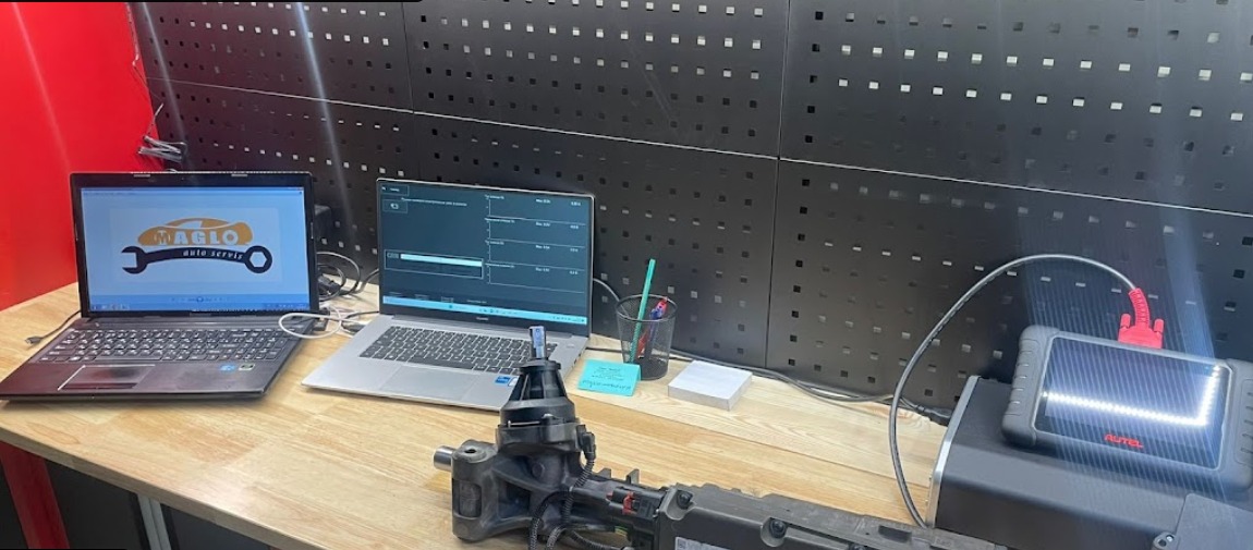 Diagnostyka samochodowa: Dwa laptopy z oprogramowaniem diagnostycznym, moduł sterujący i tester diagnostyczny Autel na stole w warsztacie.