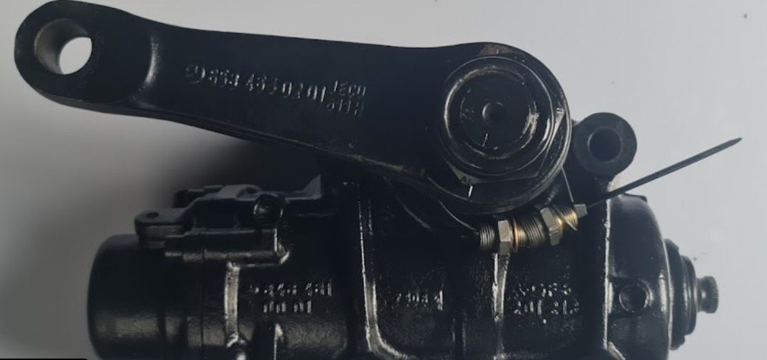 Czarna, metalowa przekładnia kierownicza z widocznymi numerami seryjnymi i elementami regulacyjnymi, zabezpieczona czarną opaską zaciskową.