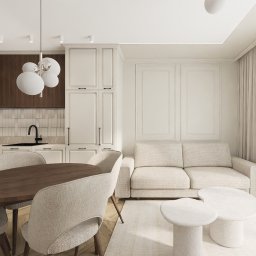 Katarzyna Wysopal - Jasne wnętrze: salon z aneksem kuchennym. Drewniany stół, beżowa sofa, białe szafki kuchenne i dekoracyjne panele ścienne. Minimalistyczny design, naturalne światło.