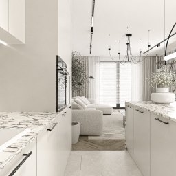 Katarzyna Wysopal - Widok na nowoczesne, otwarte wnętrze z kuchnią i salonem. Jasne szafki z marmurowymi blatami i czarnymi uchwytami. W tle beżowa sofa, duże okno i designerskie oświetlenie.