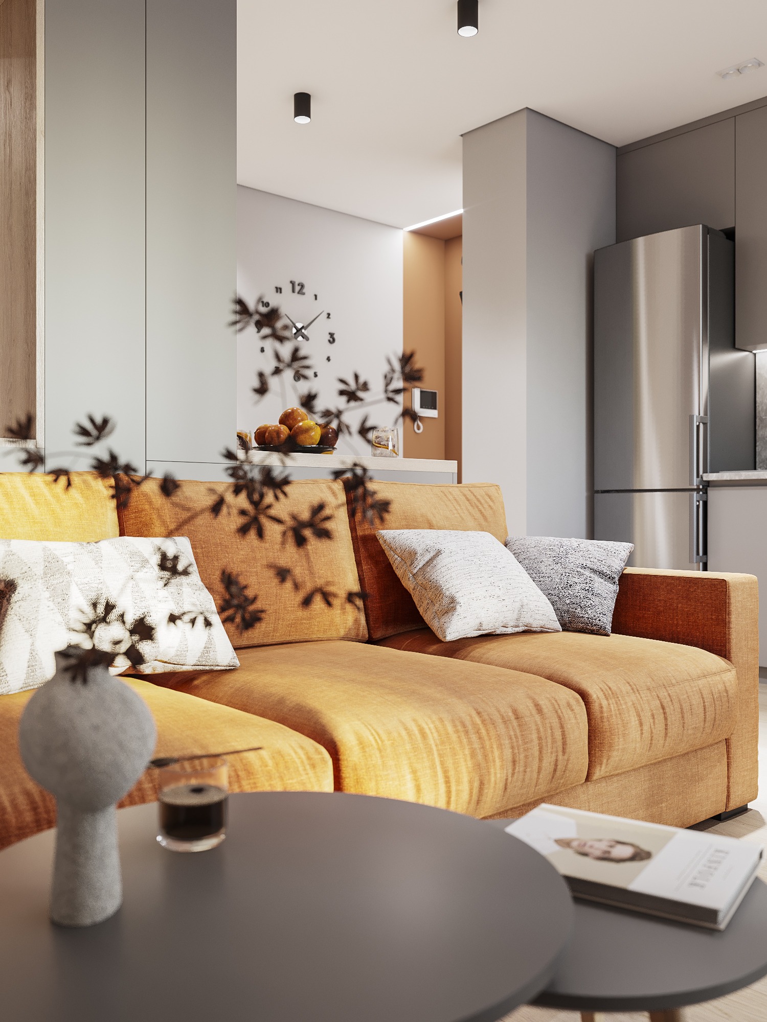 Jasnopomarańczowa sofa z poduszkami w salonie, stolik kawowy z szarą wazą i szklanką, w tle zegar ścienny i lodówka ze stali nierdzewnej.