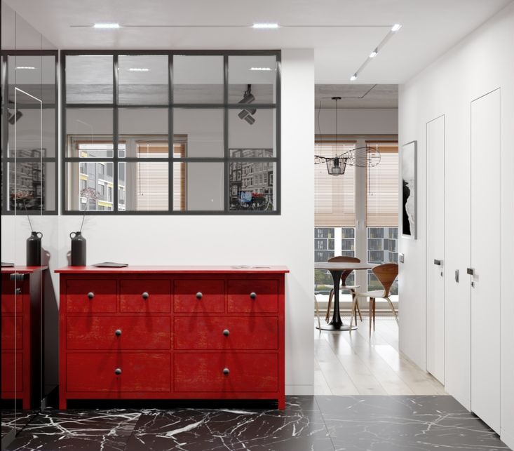 Nowoczesna kawalerka: czerwona komoda z ciemnymi gałkami na tle czarnej marmurowej podłogi, widok na jadalnię przez przeszkloną ścianę działową.