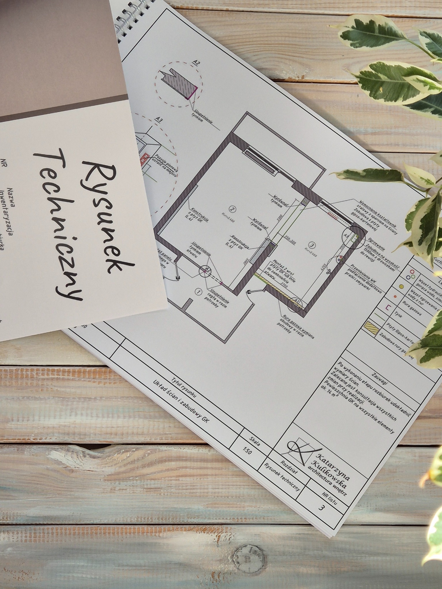 Rysunek techniczny układu ścian i zabudowy GK, skala 1:50, autorstwa Katarzyny Kulikowskiej, architektura wnętrz, leżący na drewnianym stole obok rośliny.