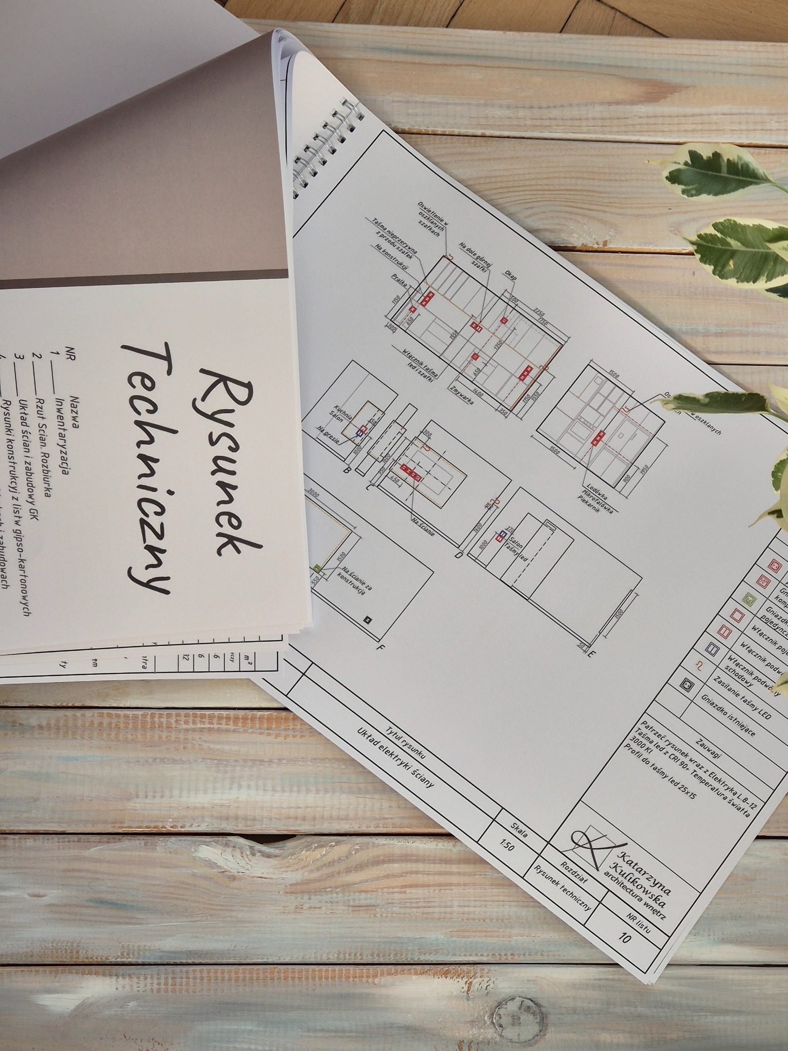 Rysunek techniczny układu elektryki ściany, z rozmieszczeniem oświetlenia LED, ułożony na drewnianym blacie, widoczny fragment rośliny.