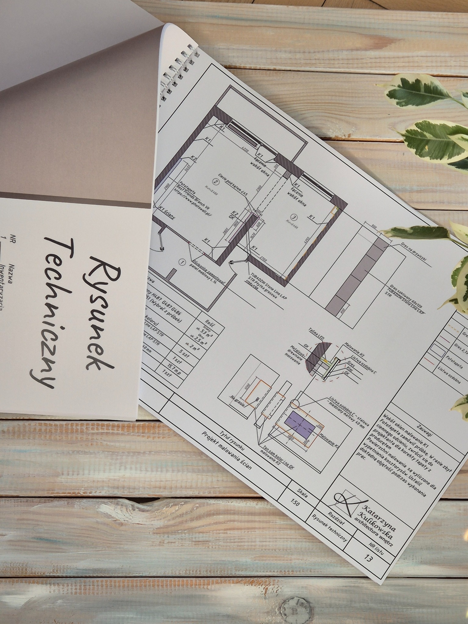 Rysunek techniczny projektu malowania ścian, z detalami wykończenia, umieszczony na drewnianym stole obok rośliny doniczkowej i notesu z napisem 'Rysunek Techniczny'.