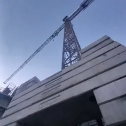 Żuraw wieżowy w trakcie montażu z widocznymi betonowymi przeciwwagami z napisem 'ZOOMLION' w pochmurny dzień.