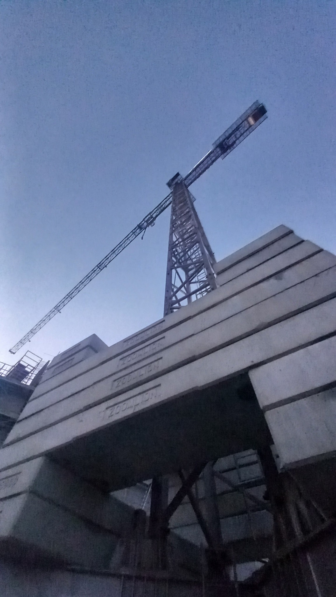 Żuraw wieżowy w trakcie montażu z widocznymi betonowymi przeciwwagami z napisem 'ZOOMLION' w pochmurny dzień.