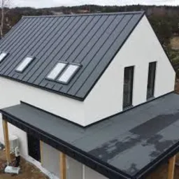 Nowoczesny dom jednorodzinny z dachem pokrytym blachą na rąbek stojący w kolorze grafitowym, z oknami dachowymi i minimalistycznym wykończeniem elewacji.