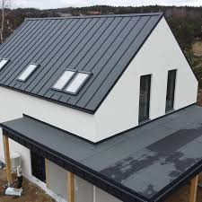 Nowoczesny dom jednorodzinny z dachem pokrytym blachą na rąbek stojący w kolorze grafitowym, z oknami dachowymi i minimalistycznym wykończeniem elewacji.