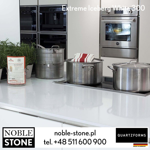 Biały blat kuchenny 'Extreme Iceberg White 300' z garnkami i ziołami na tle nowoczesnej zabudowy kuchennej. Widoczne logo Noble Stone i Quartzforms.