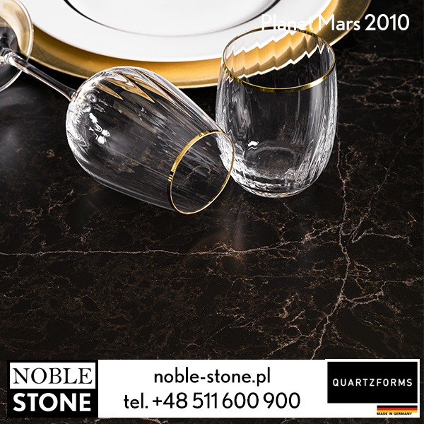 Ciemny blat kamienny 'Planet Mars 2010' z dwoma szklankami z delikatnym złotym zdobieniem, talerzem i złotą podkładką. Elegancki minimalizm.