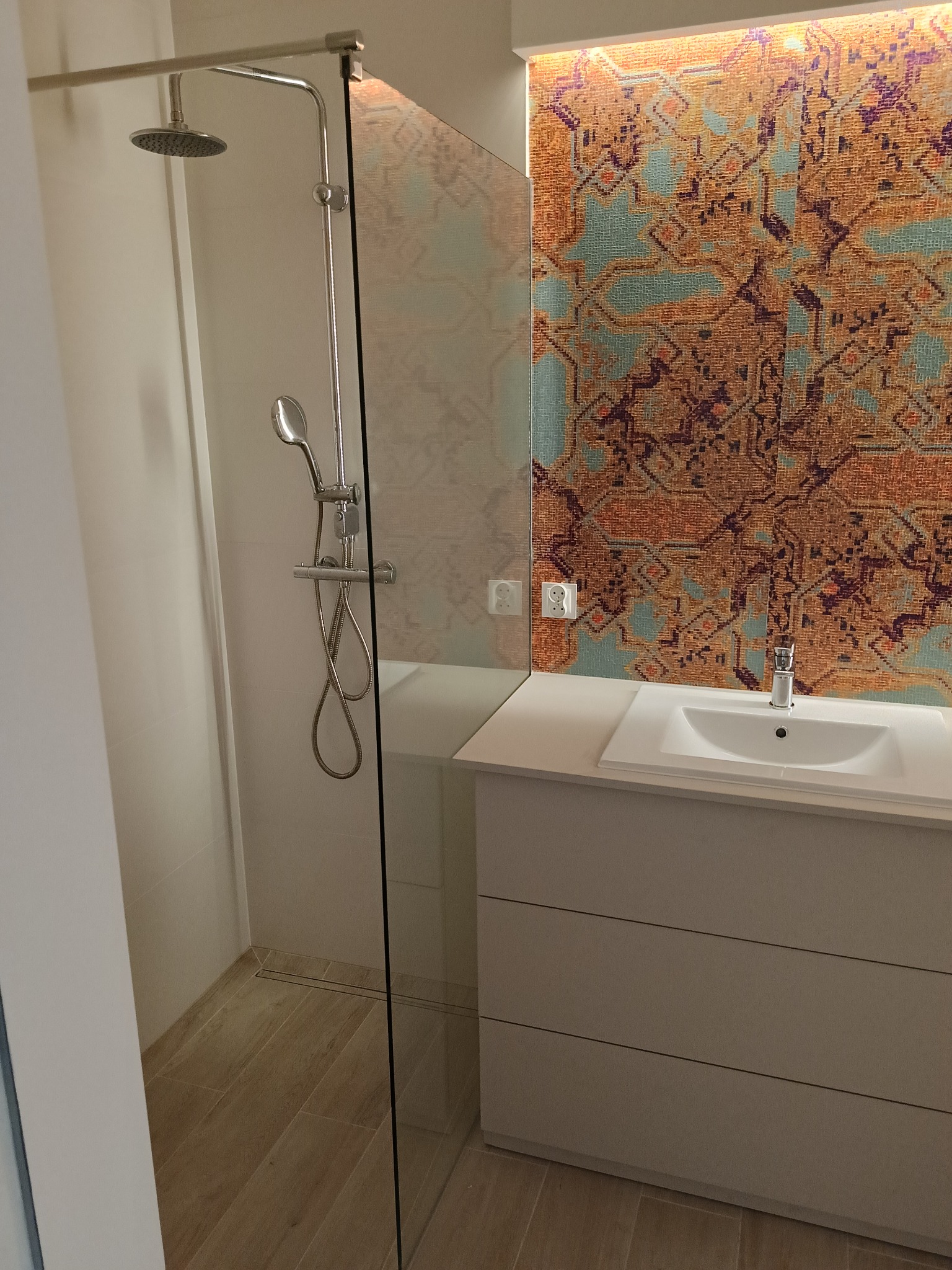 Nowoczesna łazienka z kabiną prysznicową typu walk-in, umywalką nablatową na szafce z szufladami i dekoracyjną ścianą z wzorem etnicznym podświetloną od góry.