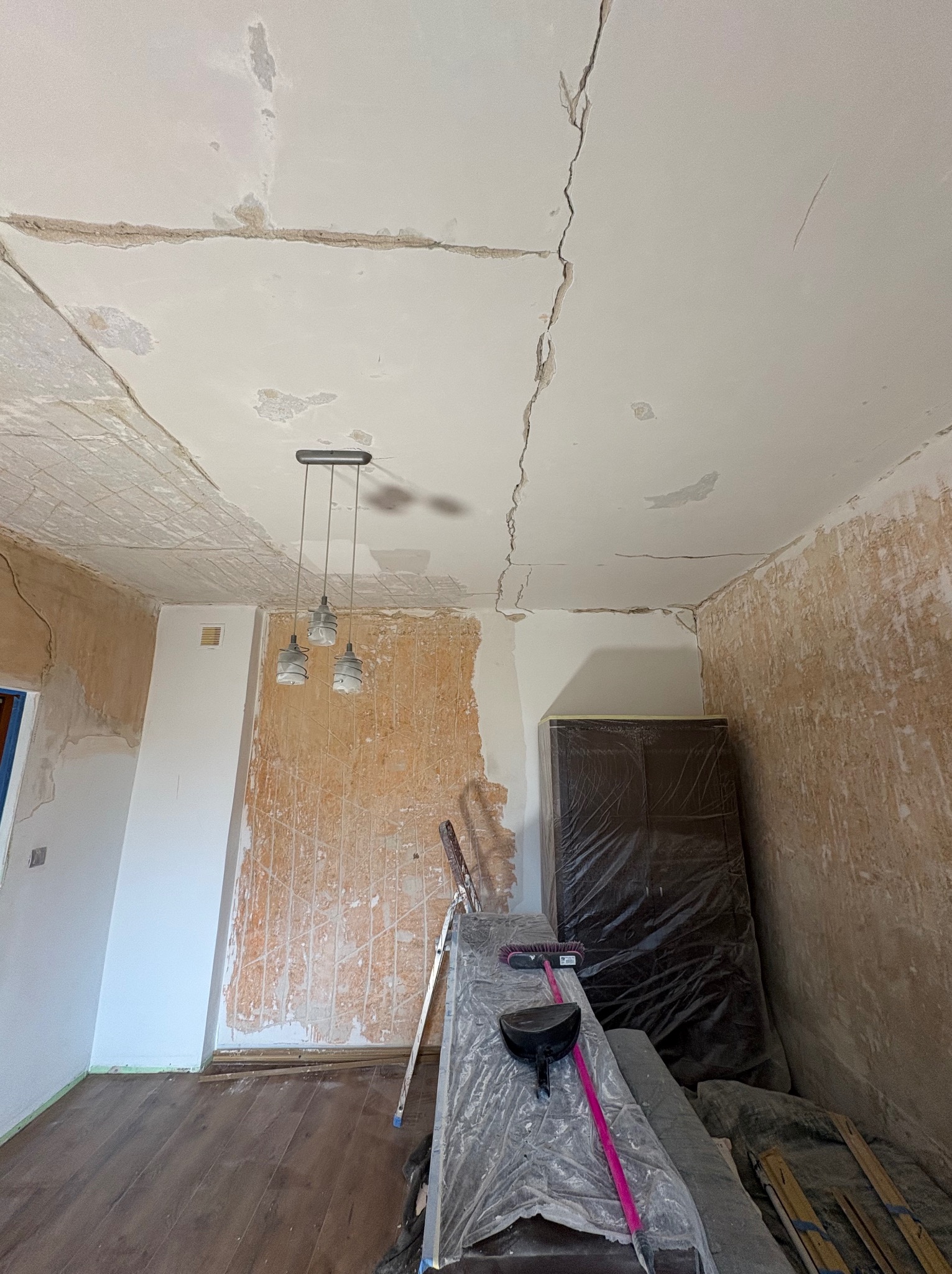 Pokój w trakcie remontu: widoczne pęknięcia na suficie, ściany częściowo przygotowane, drabina, podłoga drewniana, zabezpieczone meble.