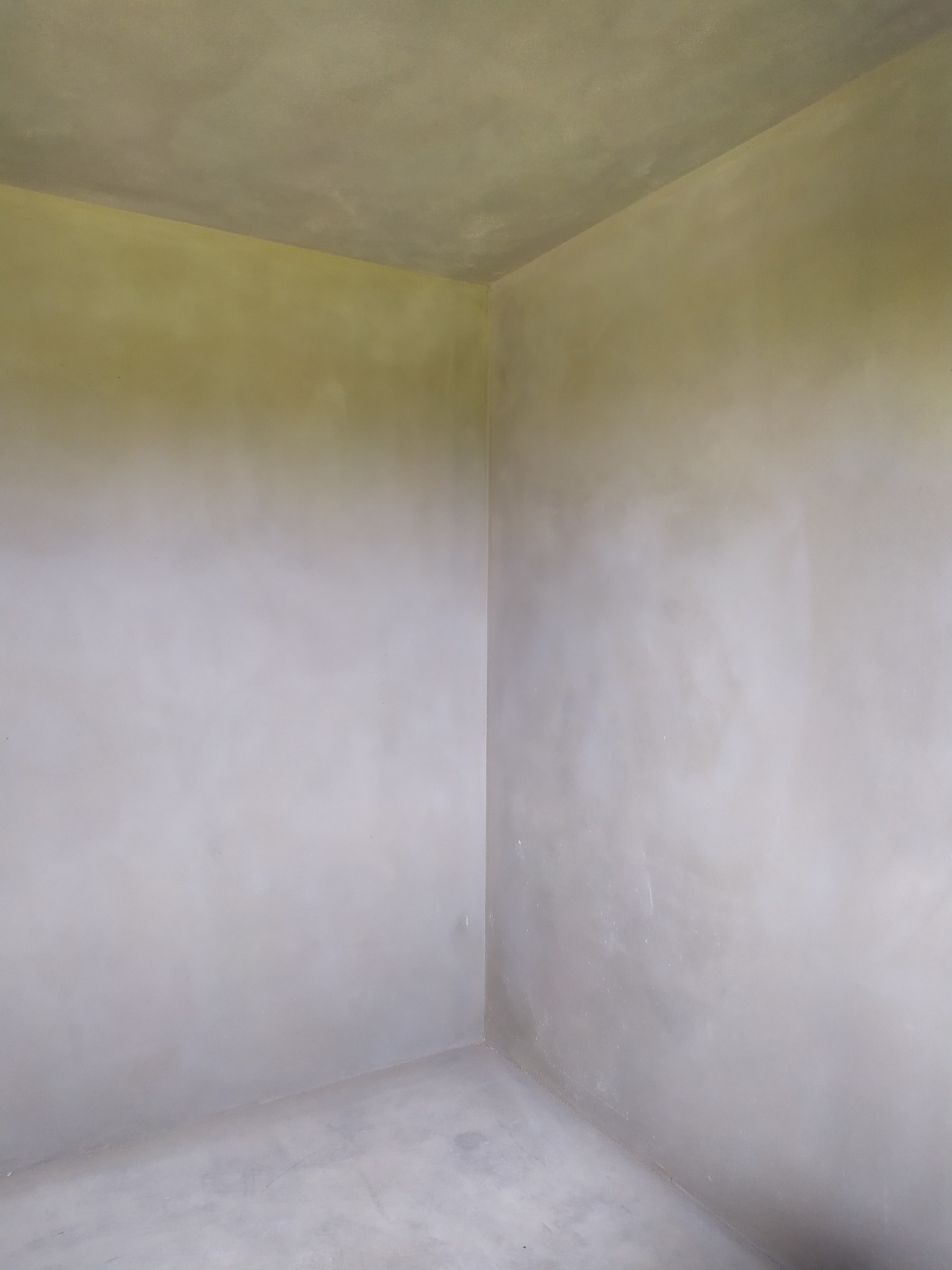 Wnętrze pokoju po nałożeniu tynku, widoczne ściany i sufit w szarym odcieniu, wykończenie surowe.