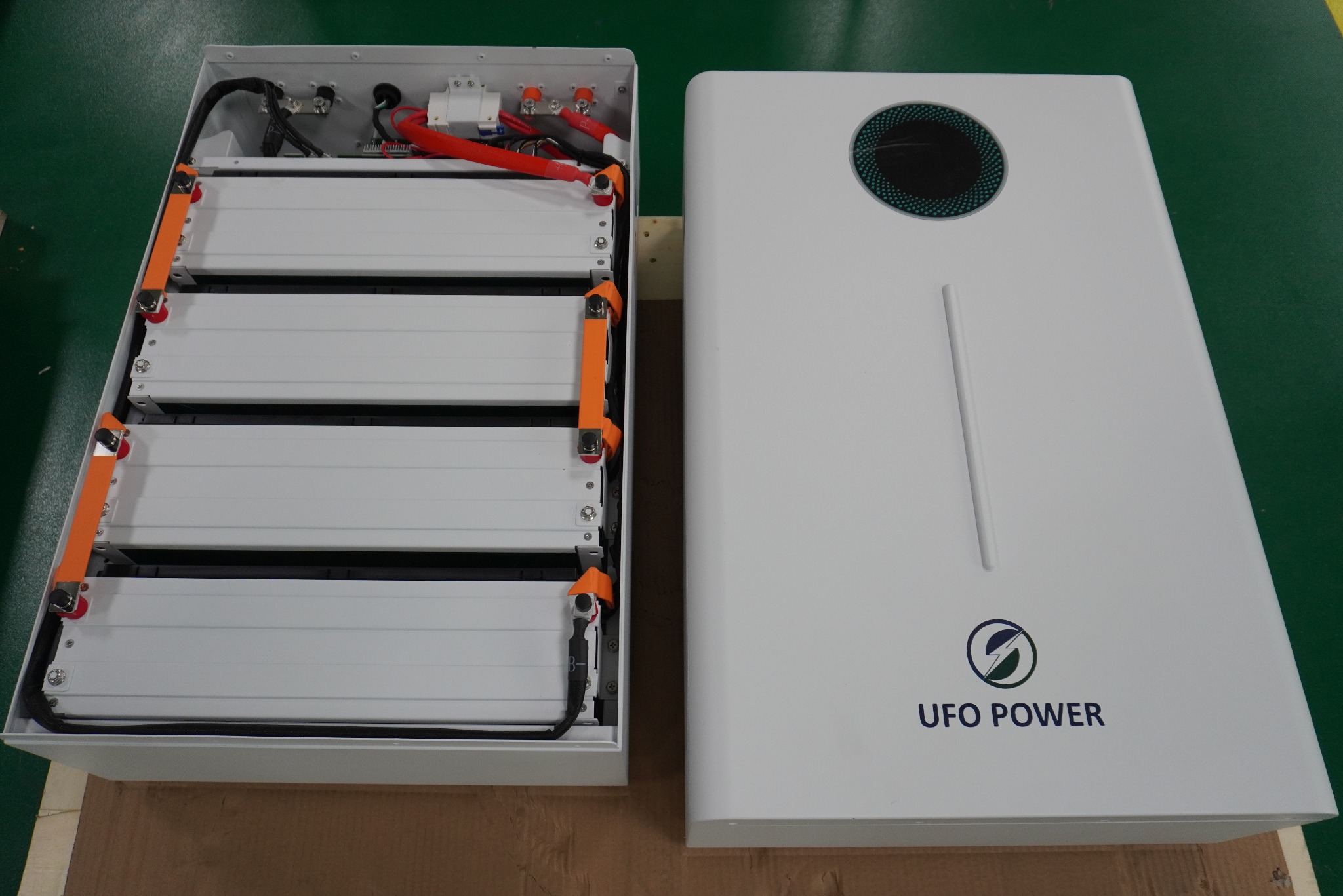 Otwarty magazyn energii UFO Power z widocznymi czterema bateriami, kablami i elektroniką, obok zamknięta obudowa z logo firmy.