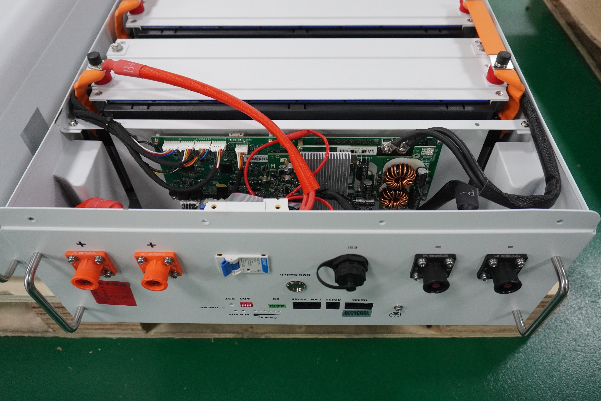 Otwarta obudowa urządzenia z elektroniką, widoczne kable, złącza i płytki drukowane, potencjalnie związane z systemem zasilania awaryjnego lub magazynem energii.