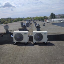 Ice Term - Dwa agregaty klimatyzacyjne Kaisai Eco zamontowane na płaskim dachu budynku, widok z góry na tle błękitnego nieba z chmurami i zabudowy miejskiej w oddali.