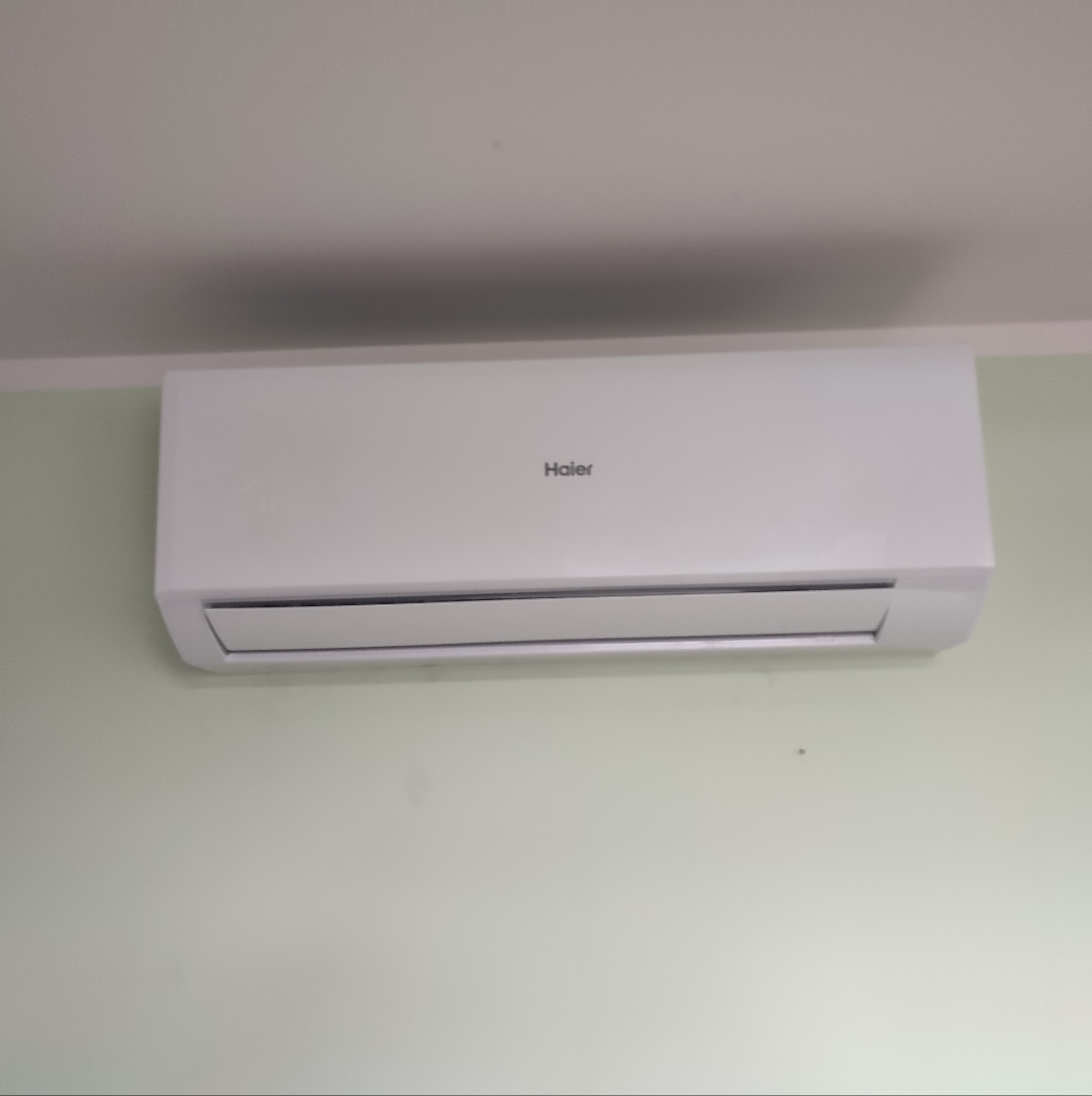 Biała klimatyzacja Haier zamontowana na jasnozielonej ścianie, widok z dołu.