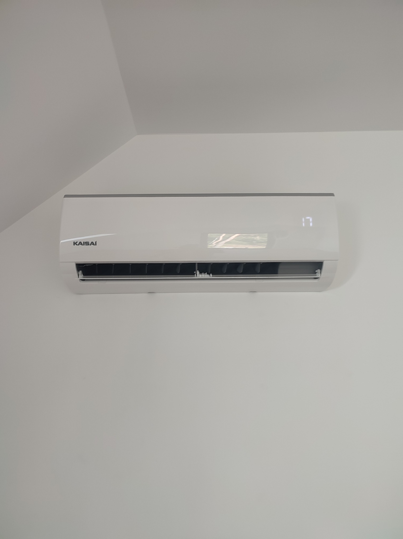 Biała klimatyzacja Kaisai z wyświetlaczem temperatury (17 stopni) zamontowana na białej ścianie pod skosem dachu.