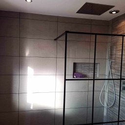 Damian building service - Nowoczesna kabina prysznicowa z czarną ramą, szare płytki imitujące kamień, półka w ścianie z fioletowym ręcznikiem i deszczownica w suficie.